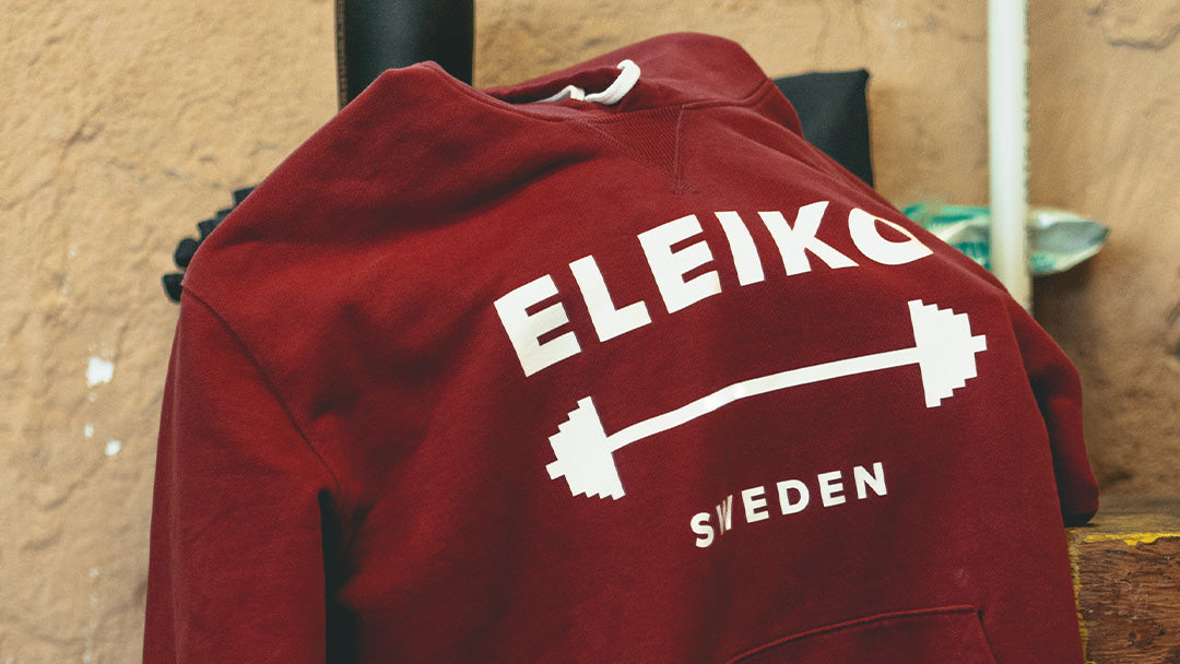 ボルドーカラーのELEIKOパーカーを斜め上から写したアパレルディテール。胸元にELEIKOロゴとバーベルデザイン、SWEDENの文字をプリント。