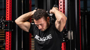 シルバーのROGUE Vグリップ ケーブルアタッチメントを使用し、オーバーヘッドトライセプスエクステンションを横後方から捉えた使用例
