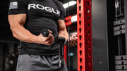 シルバーのROGUE Vグリップ ケーブルアタッチメントを使用し、トライセプスプッシュダウン開始姿勢を正面から捉えた上半身のトレーニングシーン