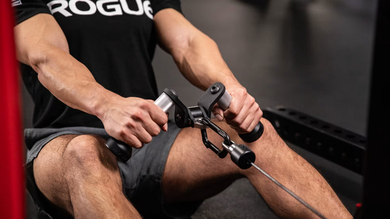シルバーのROGUE Vグリップ ケーブルアタッチメントを使用し、シーテッドローで腕を伸ばした開始姿勢を正面から捉えた使用例